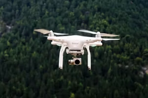 White camera drone flying over forest